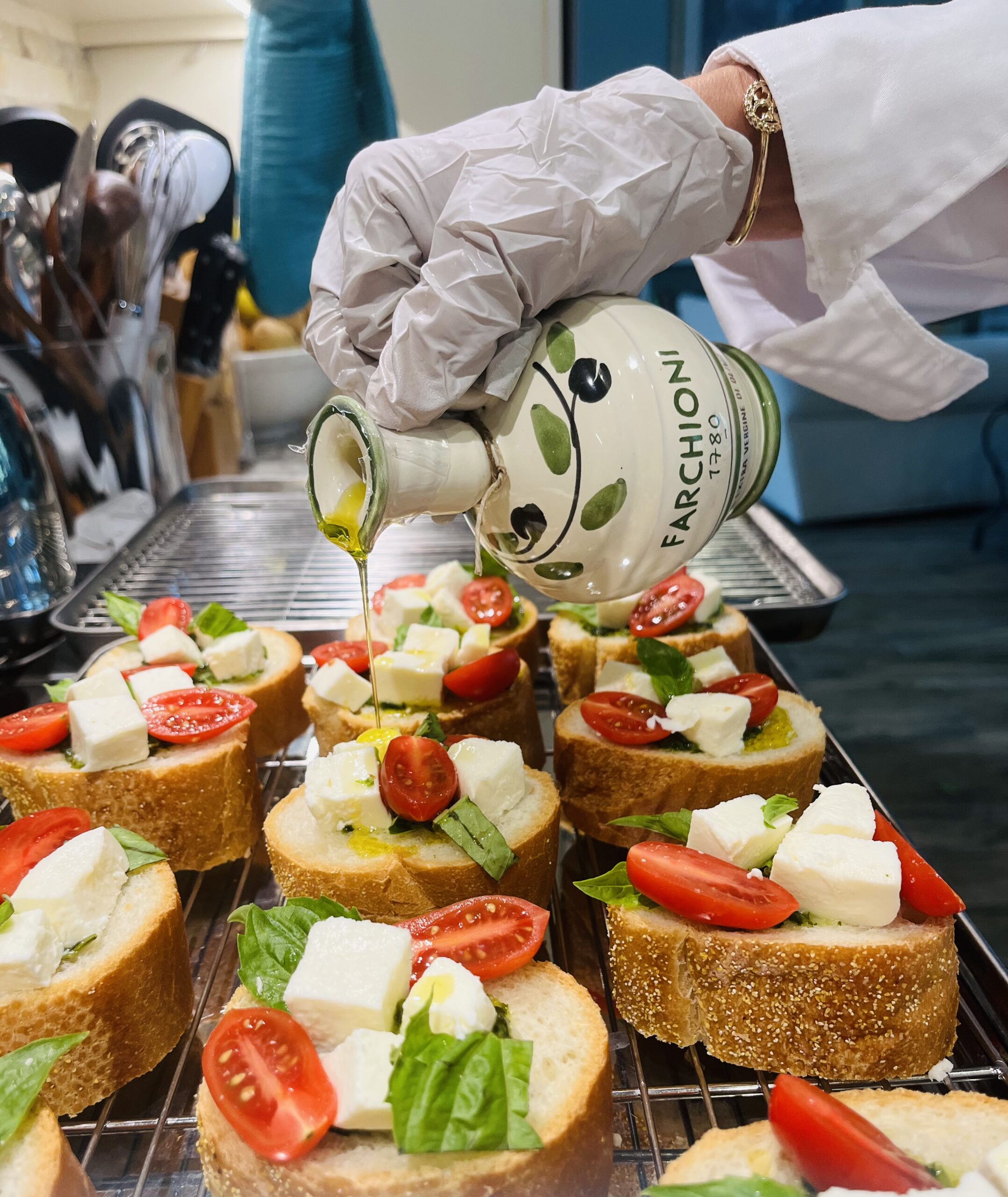 A hand pouring olive oil on bruschetta.| ANA MARIA'S CATERING