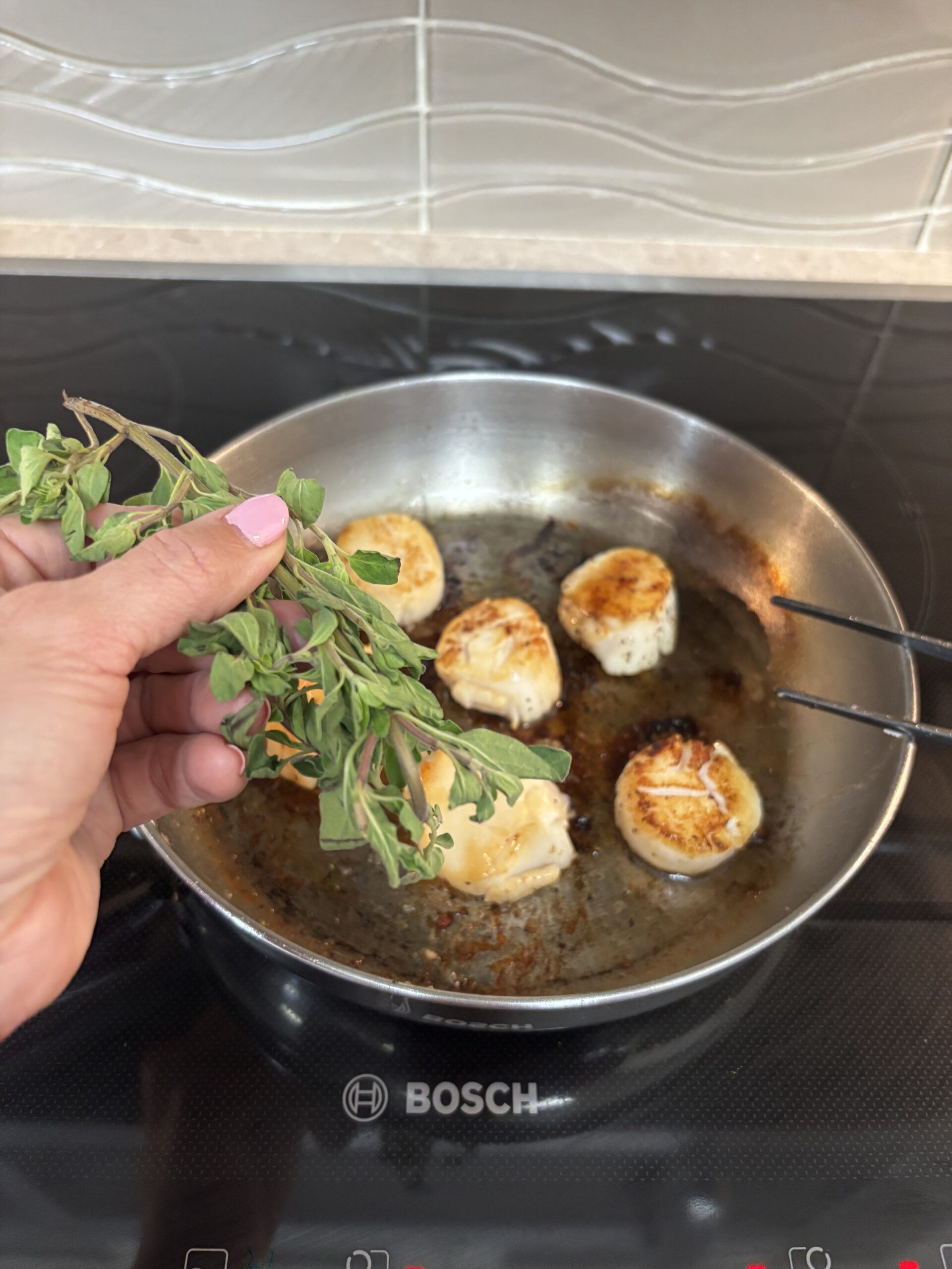 Hand adds fresh herbs to seared scallops.| ANA MARIA'S CATERING